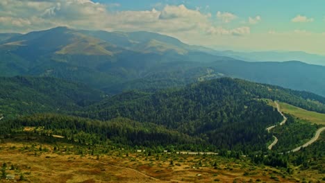 Aerial-drone-shot-view-of-a-mountain-road-with-Tarcului-mountains-in-the-background