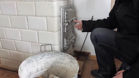 Man-brushes-off-his-dirty-hands-and-closes-door-of-an-old-home-tiled-stove