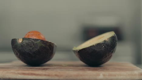 Close-up-of-avocado-fruit-cutt-off-in-half-on-wooden-cutting-board-in-kitchen