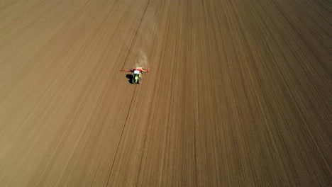 Aerial-view-of-a-green-tractor-seeding,-sowing-agricultural-crops-at-the-field-with-dust-behind