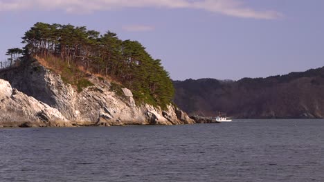 Small-fishing-vessel-passing-behind-tall-rock-cliff-and-disappearing