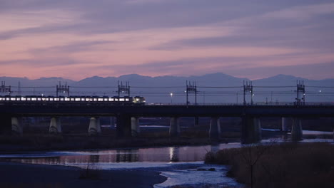 Japanischer-Zug,-Der-Am-Fluss-Futakotamagawa-Vorbeifährt,-Mit-Reflexion-Auf-Dem-Wasser-Während-Der-Schönen-Dämmerung-In-Tokio,-Japan