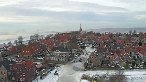 People-ice-skating-on-frozen-canal-in-idyllic-town-in-Friesland,-aerial