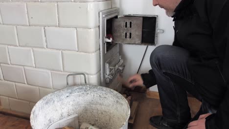 Man-puts-firewood-through-open-door-into-the-old-home-tiled-stove