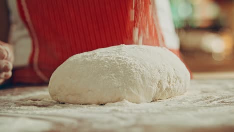 Close-up-shot-of-applying-flour-on-the-dough-by-a-woman-chef-in-a-red-apron