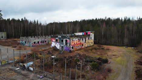 Aerial-view-of-abandoned-building-with-graffiti-in-front-of-forest-trees-in-Sweden