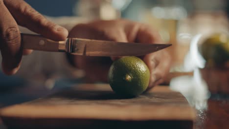 Close-up-of-male-hands-passing-by-lime-and-slicing-on-half-on-wooden-board-with-knife,-slow-motion