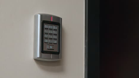 A-man's-holds-a-security-card-faub-up-to-a-numeric-keypad,-which-allows-access-to-a-locked-door-inside-a-secure-business-office