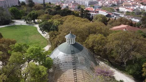 Aerial-Circular-Orbit-Flying-Over-Beautiful-Crystal-Greenhouse-In-Historical-Park-In-Downtown-Lisbon,-Portugal