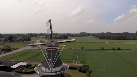 Typische-Holländische-Windmühle-Mit-Dochten-In-Der-Landschaft-Der-Niederlande-Von-Hinten-Gesehen,-Die-Sich-Schließen,-Um-Die-Breitere-Flache-Landwirtschaftslandschaft-Zu-Zeigen