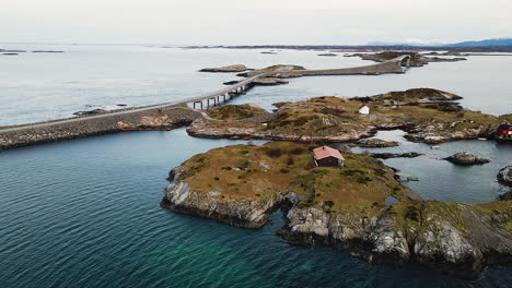 Boathouse-On-Rocky-Island-With-Storseisundet-And-Hulvagen-Bridge-At-The-Atlantic-Ocean-Road-In-Norway