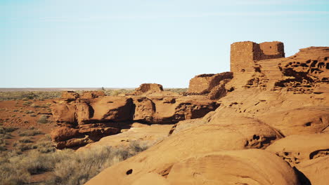 Still-shot-with-red-sandstone-rock-formations-in-foreground-and-Wukoki-Pueblo-ruins-in-background