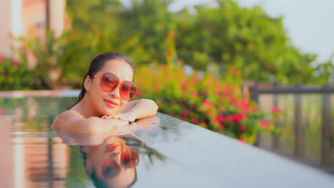 Stunning-Asian-Female-Relaxing-at-Border-of-Infinity-Pool-Smiling-and-Looking-at-Camera