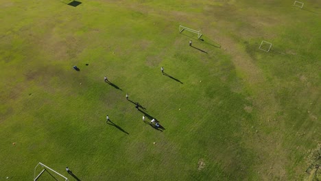 Toma-Aérea-De-Drones-Que-Muestra-A-Un-Equipo-De-Niños-Jugando-Fútbol-En-Césped-Verde-Durante-El-Verano