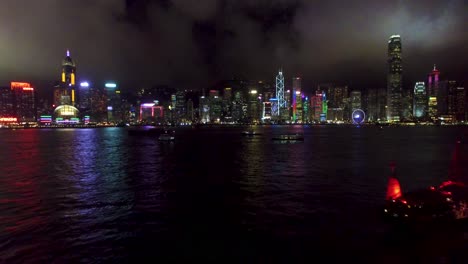Vista-Aérea,-Panorama-Del-Paisaje-Urbano-Nocturno-De-Hong-Kong-Y-Frente-Al-Mar,-Edificios-Brillantes-En-La-Bahía,-Disparo-De-Drones