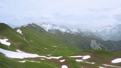 Vista-Aérea-De-Las-Verdes-Montañas-De-Los-Alpes-Con-Algo-De-Nieve-Durante-El-Verano