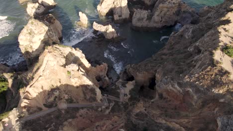 Boardwalk-with-steep-steps-from-top-cliff-lead-down-to-rocky-sheltered-beach,-Lagos,-Algarve