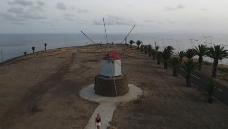 Female-traveler-walks-at-historic-windmills-of-Porto-Santo,-aerial