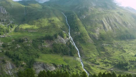 Aerial-view-of-a-river-running-down-through-the-green-mountains-of-the-Alps