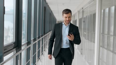 Business-adult-man-walking-down-the-hall-receives-a-joyful-message-on-a-smartphone