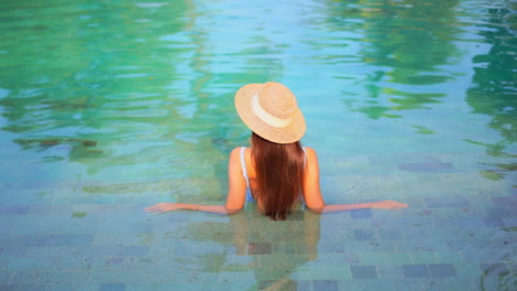Back-of-lonely-woman-with-long-hair-and-floppy-hat-enjoying-in-pool-water-on-hot-summer-day,-full-frame