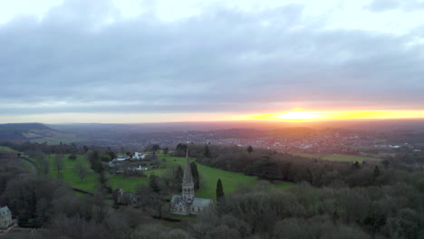 An-aerial-shot-around-an-old-English-church-on-a-hill-in-Ranmore-common,-in-Dorking-at-sunrise