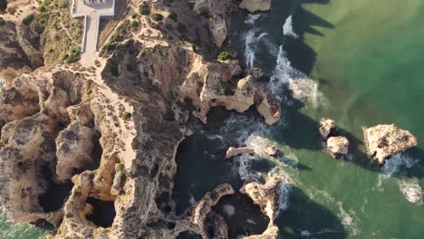 Cinematic-aerial-bird-eye-view-of-rocky-formations-located-in-Praia-dos-Estudantes-Algarve,-Portugal