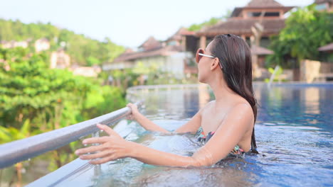 A-pretty-young-woman-makes-her-way-to-the-infinity-edge-of-the-pool-that-looks-over-the-green-tropical-paradise