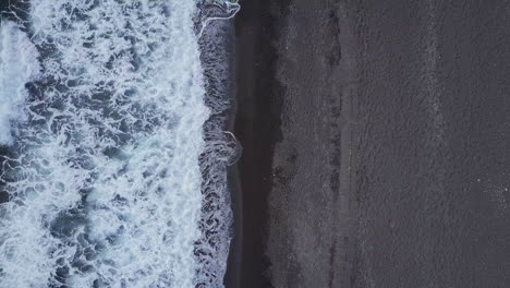 Aerial-looking-down-at-waves-coming-in-to-black-sand-beach-in-Mediterranean