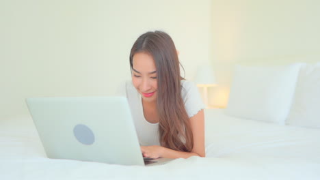 Close-up-of-an-attractive-woman-working-on-her-laptop-as-she-lays-on-a-big-comfortable-bed