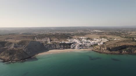 Cinematic-aerial-view-turquoise-sea-and-old-fishing-village-with-whitewashed-cottages-houses-in-Burgau-Portugal