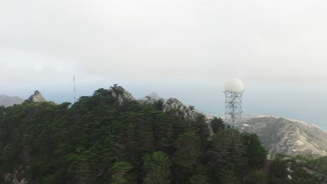 Radar-tower-on-top-of-mountain-in-Porto-Santo-in-clouds,-aerial