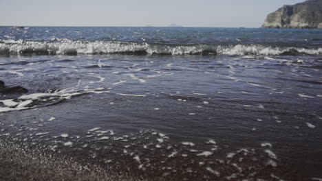 Slow-motion-shot-of-waves-rolling-onto-black-sand-beach-on-bright-day