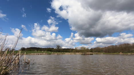 White-clouds-pass-by-over-head-at-a-man-made-Trout-Fishing-pool-in-Worcestershire,-England,-UK