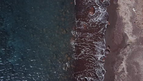 Top-down-aerial-shot-over-red-sand-beach-on-Greek-island-of-Santorini,-4K