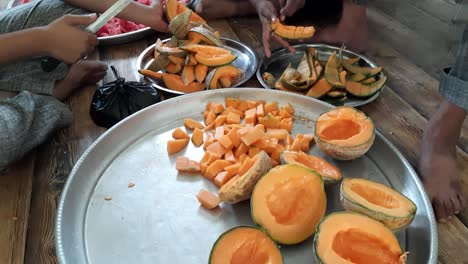 Hands-of-a-senior-man-using-two-knives-to-cut-fresh-delicious-cantaloupe-muskmelon-in-big-plates,-A-man-cuts-a-melon-into-slices,-cubes-in-a-plate