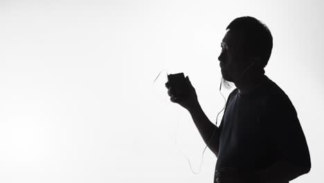 Silhouette-of-a-man-listening-to-music-on-a-smartphone,-vintage-tape-player-or-smart-device