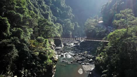 Luftflug-Des-Natürlichen-Felsigen-Stroms-Und-Des-Touristen,-Der-Während-Des-Sonnigen-Tages-Im-Nationalpark-Des-Bezirks-Wulai-In-Taiwan,-Asien,-über-Die-Brücke-Geht
