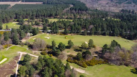 Rotating-Aerial-Over-Golf-Course-Revealing-Dark-Green-Forest-And-Farmhouse-In-Distance