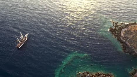 Drone-Ver-Video-De-Un-Hermoso-Barco-De-Vela-Navegando-En-El-Mar-Egeo-Azul-Profundo-Durante-La-Puesta-De-Sol,-Santorini,-Grecia