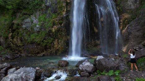 Tourist-woman-taking-picture-on-beautiful-mountain-waterfall-in-Theth,-Albania