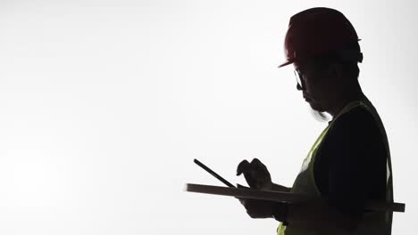 Silhouette-of-an-engineer-with-blueprints-and-tablet-in-hand-working-on-a-construction-project