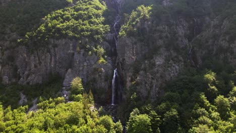 Waterfall-in-the-middle-of-rocky-mountain-slope-revealed-after-green-trees-of-forest-in-Theth,-Albania