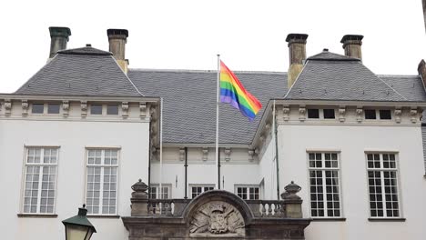Rainbow-colored-LGBTQ+-flag-on-top-of-historic-facade-of-city-hall-in-Zutphen,-The-Netherlands,-waving-gently-in-support-of-community