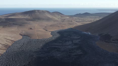 Black-basalt-rock-slow-moving-lava-stream-stretching-towards-ocean,-Iceland