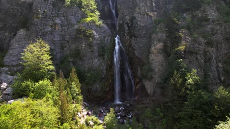 Tourists-visiting-beautiful-waterfall-of-Theth,-hiking-on-mountains-in-Albanian-Alps
