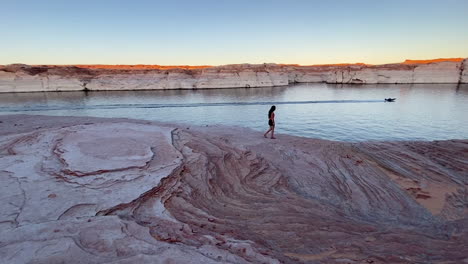 Lonely-Female-Walking-on-Layered-Sandstone-Pattern,-Coast-of-Lake-Powell,-Sunset-Landscape-and-Unique-Texture,-Panorama