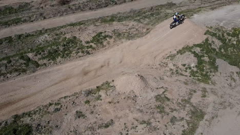 Aerial-shot-of-motocross-rider-coming-around-turn-and-hitting-jump