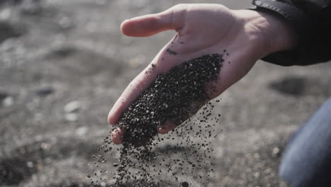Black-sand-of-Perissa,-Greece-slowly-falling-out-of-mans-hands,-slow-motion