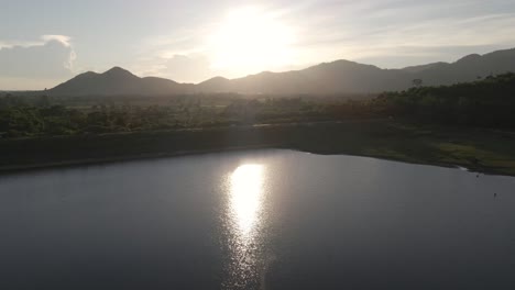 4K-Luftaufnahmen-Im-Tiefflug-Mit-Hellem-Sonnenlicht,-Das-Sich-Im-Wasser-Am-Khlong-Bod-Reservoir-In-Nakhon-Nayok,-Thailand,-Widerspiegelt